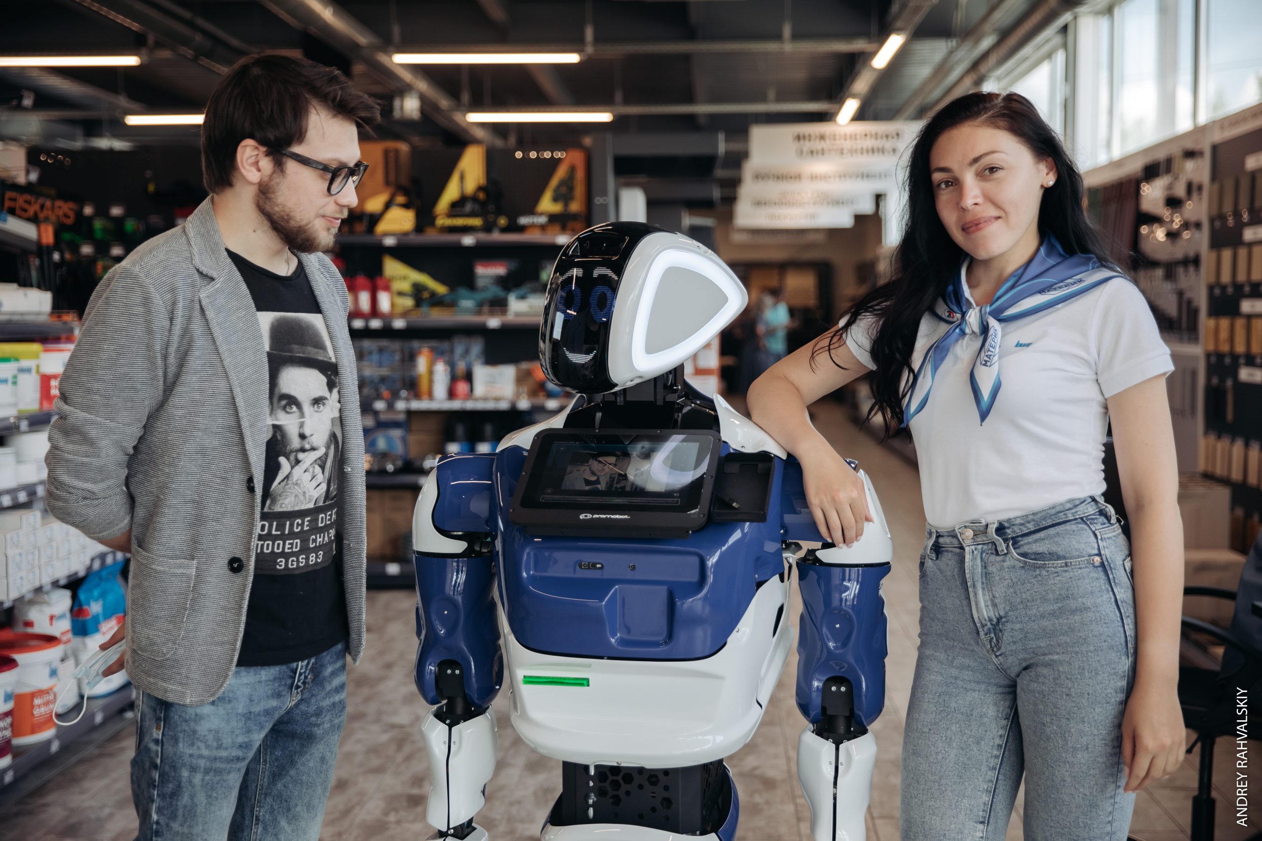 Робот промобот с мужчиной и женщиной среди полок строительного магазина